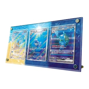 May include: A rectangular acrylic display frame featuring a blue water-themed background with three Japanese Pokémon trading cards: Squirtle, Wartortle, and Blastoise ex. The frame is secured with four silver-toned metal corner bolts.