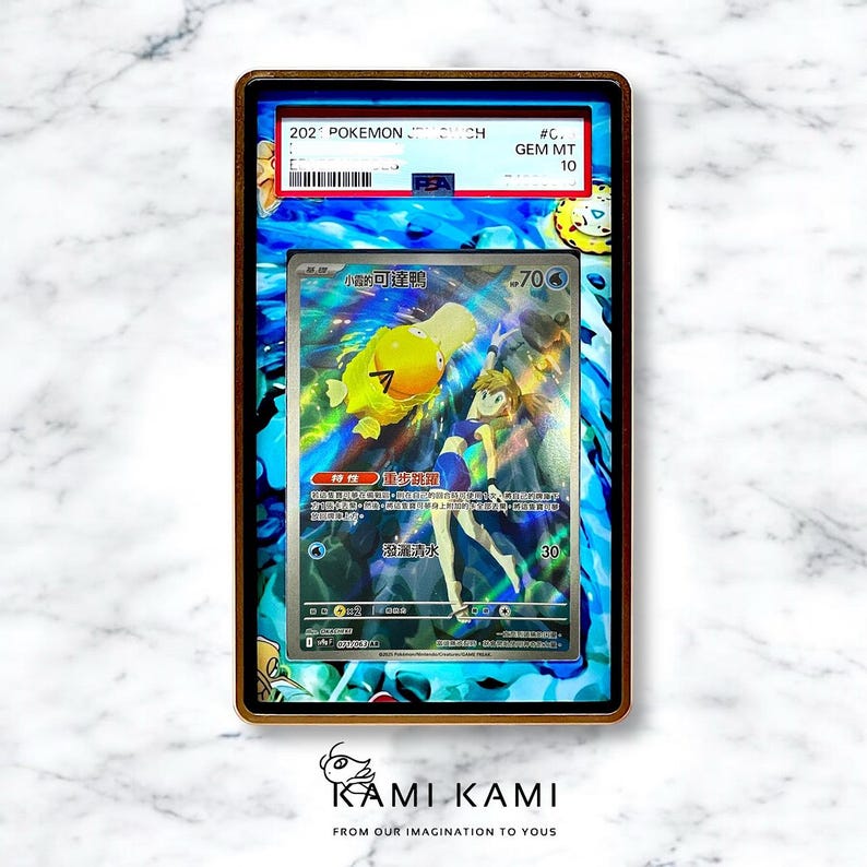 May include: A framed Pok&eacute;mon trading card featuring a yellow Psyduck character and a female trainer. The card is graded GEM MT 10. The frame has a gold border and a blue and white patterned background.
