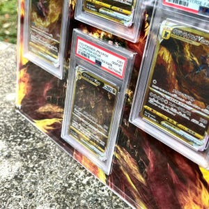 Puede incluir: Se muestran varias cartas coleccionables de Pok&eacute;mon clasificadas, con ilustraciones vibrantes y texto japon&eacute;s. Las cartas est&aacute;n dentro de protectores transparentes, con etiquetas que indican los detalles de la carta y la informaci&oacute;n de clasificaci&oacute;n. El fondo presenta un dise&ntilde;o abstracto y ardiente.