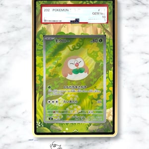 May include: A PSA graded Rowlet Pokemon trading card encased in a gold-rimmed protective slab. The card features a brown and white owl-like creature in a green forest setting with Japanese text, 80 HP, and a Gem Mint 10 grade label at the top.