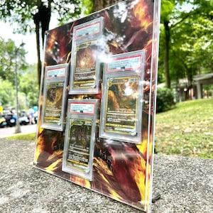 Puede incluir: Una pantalla acr&iacute;lica transparente con cinco cartas coleccionables calificadas. El fondo presenta un dise&ntilde;o ardiente, naranja y amarillo. Las cartas est&aacute;n encerradas en protectores, con informaci&oacute;n de calificaci&oacute;n visible.