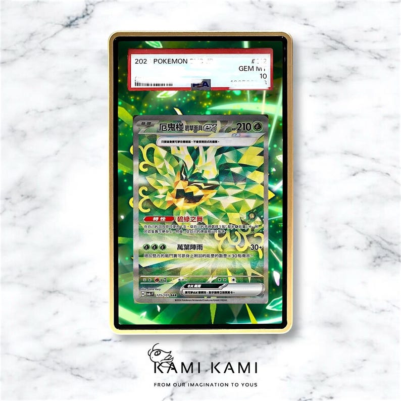 May include: A framed Pok&eacute;mon trading card featuring a green and yellow illustration of a creature. The card is graded and encased in a gold-colored frame. The card has Japanese text and the number 210.