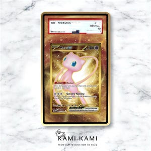 May include: A gold-colored Pokemon trading card featuring a pink Mew EX character. The card is encased in a gold frame with the text "202 Pokemon" and "GEM M 10". The card has the text "Mew EX" and "Genome Hacking". The bottom of the frame has the text "KAMI KAMI".