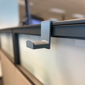 May include: A grey plastic hook designed to hang items on a cubicle wall.