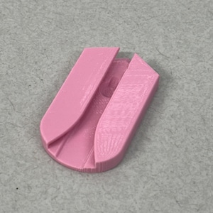 May include: A light pink, 3D-printed object with a curved design. The object has a rounded base and two upright, angled sections. The design appears to be a small, functional item, possibly a holder or clip.
