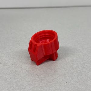 May include: A bright red, 3D-printed object with a cylindrical top and a geometric base. The object has a textured surface and appears to be a small, hollow component, possibly a part of a larger assembly. The design suggests a mechanical or technical application.