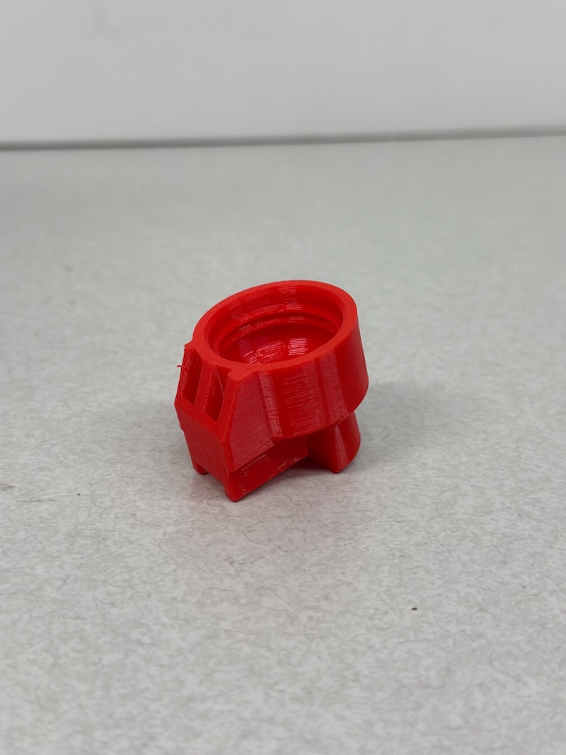 May include: A bright red, 3D-printed object with a cylindrical top and a geometric base. The object has a textured surface and appears to be a small, hollow component, possibly a part of a larger assembly. The design suggests a mechanical or technical application.