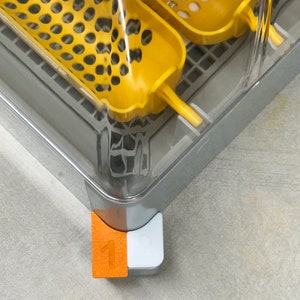 May include: A clear plastic container with two yellow plastic trays inside. The trays have a grid pattern and are labelled with numbers. The container has a white and orange number "1" on the bottom.