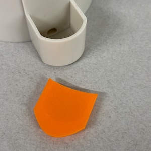 May include: A bright orange, curved, foam piece. The piece is shaped like a small, rounded, upside-down U.