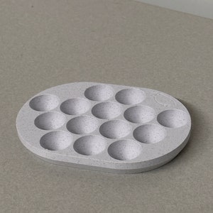 May include: A light gray silicone tray with 16 round indentations. The tray is speckled with white flecks.