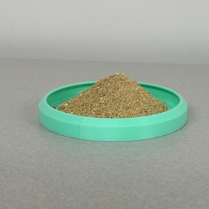 May include: A small pile of brown spice sits in a light green plastic dish.