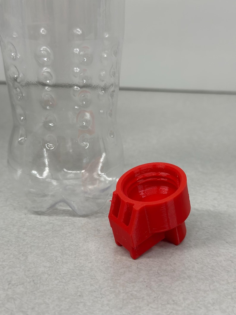 May include: A clear plastic bottle with a textured surface and a bright red 3D-printed cap. The cap is cylindrical with a geometric design. The bottle is empty and has a standard shape.