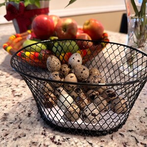May include: A black wire basket filled with speckled quail eggs on a white countertop.