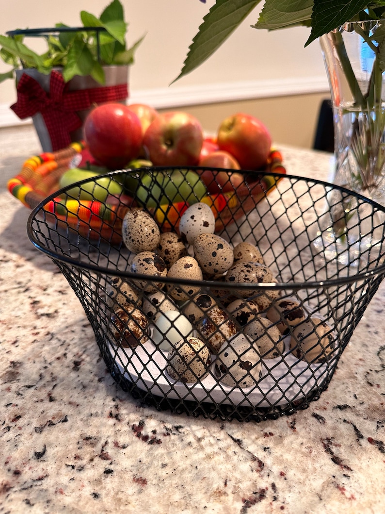 May include: A black wire basket filled with speckled quail eggs on a white countertop.