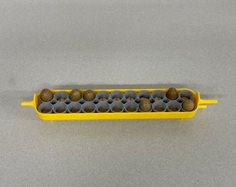 Puede incluir: Un porta huevos de plástico amarillo con inserciones grises, que contiene varios huevos moteados. El soporte tiene forma rectangular con bordes redondeados y asas. Los huevos son de varios tonos de marrón y beige.