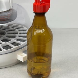 May include: A clear, brown plastic bottle with a red cap. The bottle contains a clear liquid. The cap is a bright red color. The bottle has a label with the text "019 OR 10C".