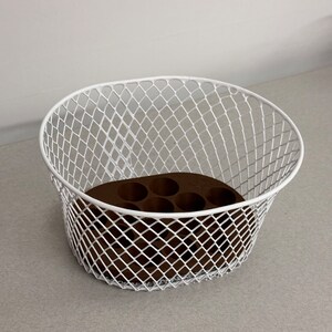 May include: White metal wire basket with a brown plastic insert with six round holes. The basket is oval shaped and has a diamond pattern.