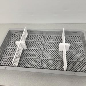 May include: A grey plastic storage container with a grid pattern and white dividers. The container is rectangular with rounded corners and small holes. White dividers are arranged in a cross shape, designed to separate items.