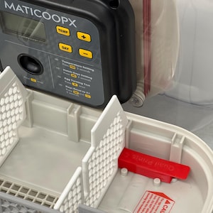 Può includere: Un'incubatrice per uova in plastica bianca con un pannello di controllo digitale etichettato "MATICOOOPX". Il pannello di controllo ha pulsanti per la temperatura, il giorno e la rotazione delle uova. L'incubatrice ha un coperchio in plastica trasparente e una maniglia in plastica rossa.