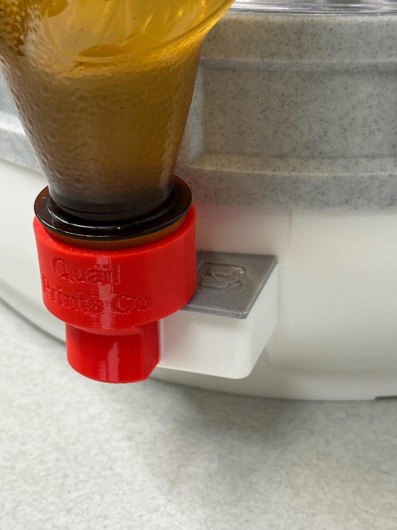 May include: A red 3D-printed adapter with the text "Quail Prints Co" attached to a clear glass bottle. The adapter is connected to a white and gray container. The bottle contains a brown liquid.