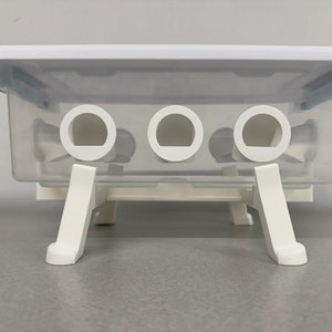 May include: A clear plastic storage container with three compartments and a white lid. The container has a white base with three legs.