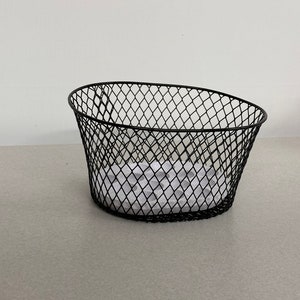 May include: Black wire basket with a white paper insert. The basket is oval shaped and has a wire mesh design.