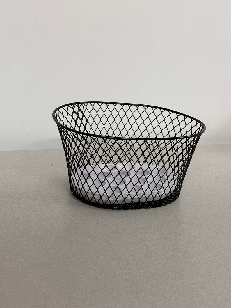 May include: Black wire basket with a white paper insert. The basket is oval shaped and has a wire mesh design.