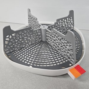 May include: A white and gray baby bottle sterilizer with a removable, gray, mesh basket. The sterilizer has a gray base with a circular, gray, mesh insert. The sterilizer has a red and orange button on the side.