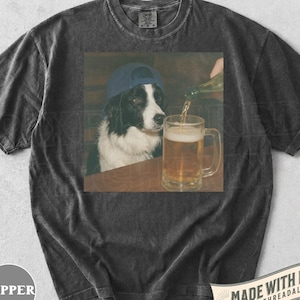 May include: Dark grey t-shirt with a graphic of a Border Collie wearing a blue cap, watching a beer mug being filled. The shirt has the word "PEPPER" printed on the bottom left and "MADE WITH LOVE" on the bottom right.