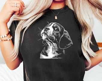 May include: Black and white illustration of a beagle dog looking up. The illustration is printed on a black t-shirt.