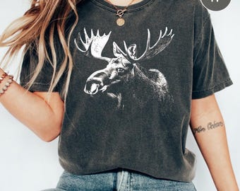 May include: Dark gray t-shirt featuring a detailed white graphic of a moose head with large antlers. The shirt has a vintage, worn look. The word "Pepper" is printed on the upper right side of the shirt.