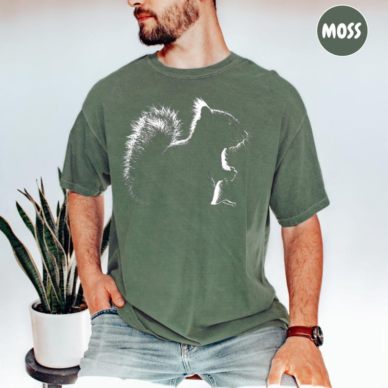 A man wearing a green t-shirt with a white squirrel graphic is sitting next to a potted plant.