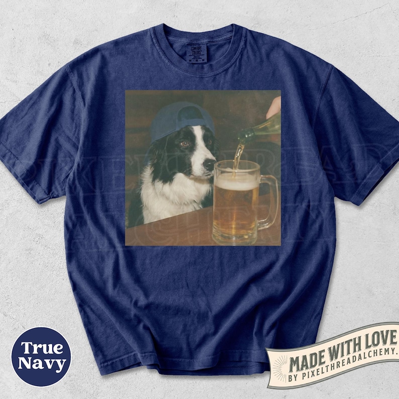 May include: Navy blue t-shirt with a graphic of a Border Collie wearing a blue baseball cap, watching beer being poured into a glass. The shirt has a round neck and short sleeves. The words "MADE WITH LOVE" are printed on the bottom right.