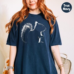 A woman with long red hair wearing a navy blue t-shirt with a white silhouette of a squirrel on it.