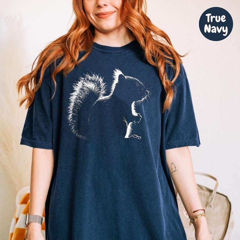 A woman with long red hair wearing a navy blue t-shirt with a white silhouette of a squirrel on it.