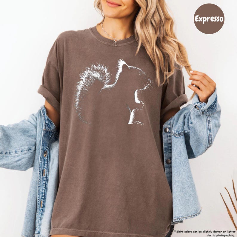 A woman wearing a brown t-shirt with a white squirrel graphic and a denim jacket, smiling and posing for the camera.