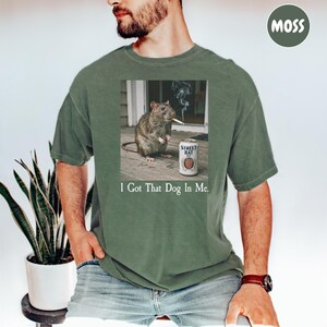 A man wearing a green t-shirt with a graphic of a rat smoking a cigarette and the text "I Got That Dog In Me."