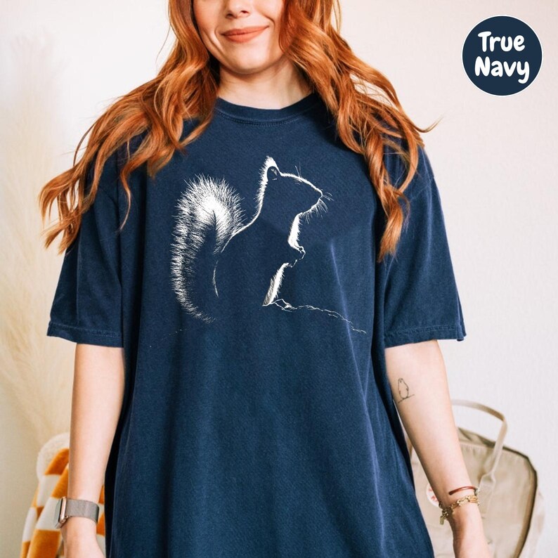 A woman with long red hair wearing a navy blue t-shirt with a white silhouette of a squirrel printed on it.