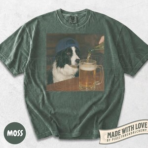May include: Moss green t-shirt with a graphic of a Border Collie wearing a blue baseball cap, watching a beer mug being filled. The shirt has a vintage look. The text "MADE WITH LOVE" is visible.