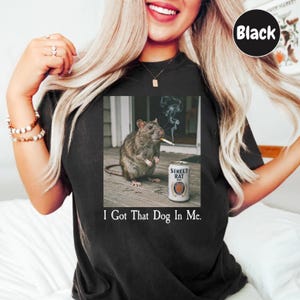 A woman wearing a black t-shirt with a graphic of a rat smoking a cigarette and the text "I Got That Dog In Me."