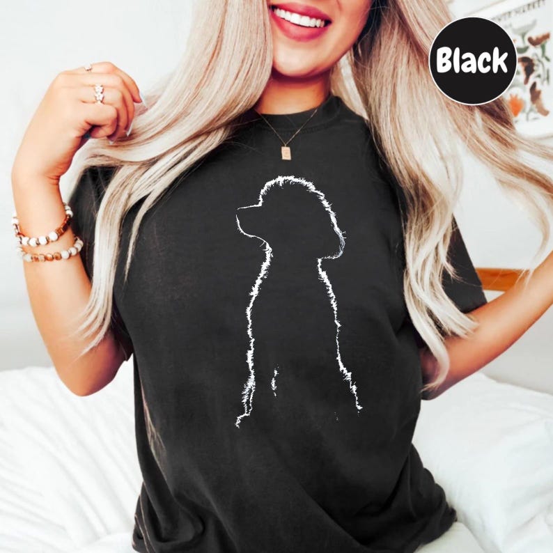 A woman with long blonde hair is smiling and posing for a photo, wearing a black t-shirt with a white silhouette of a dog.