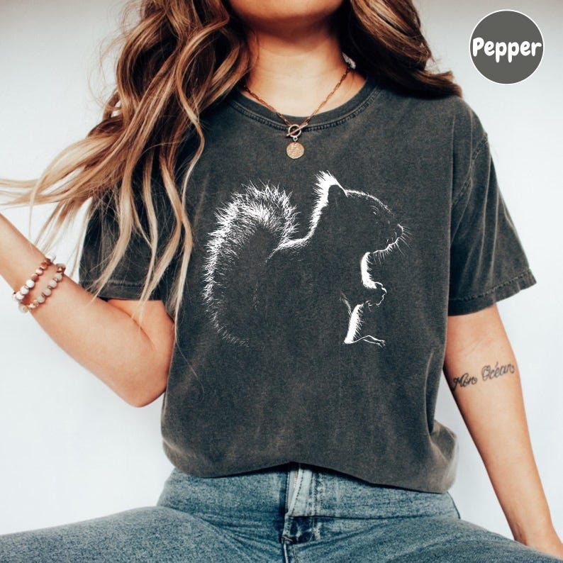 A woman wearing a gray t-shirt with a white graphic of a squirrel, paired with blue jeans, and accessorized with bracelets and a necklace.