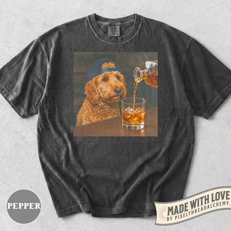 K&ouml;nnte beinhalten: Dunkelgraues T-Shirt mit einem quadratischen Grafikdesign. Die Grafik zeigt einen Golden Doodle mit blauer Kappe, der ein Glas Whiskey mit Eis betrachtet. Whiskey wird in das Glas gegossen. Das T-Shirt hat einen Vintage-Look.