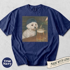 May include: Navy blue t-shirt featuring a graphic of a white dog wearing a baseball cap, looking at a beer mug being filled. The shirt has the words "True Navy" and "Made with Love" printed on it.