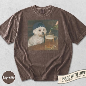 May include: Brown t-shirt with a graphic of a white dog wearing a blue baseball cap, sitting at a table while beer is poured into a mug. The shirt has a vintage, washed look. The text "Made with Love" is printed on the bottom right.