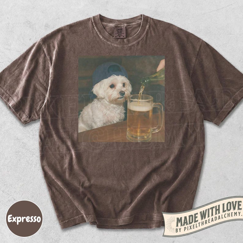 May include: Brown t-shirt with a graphic of a white dog wearing a blue baseball cap, sitting at a table while beer is poured into a mug. The shirt has a vintage, washed look. The text "Made with Love" is printed on the bottom right.