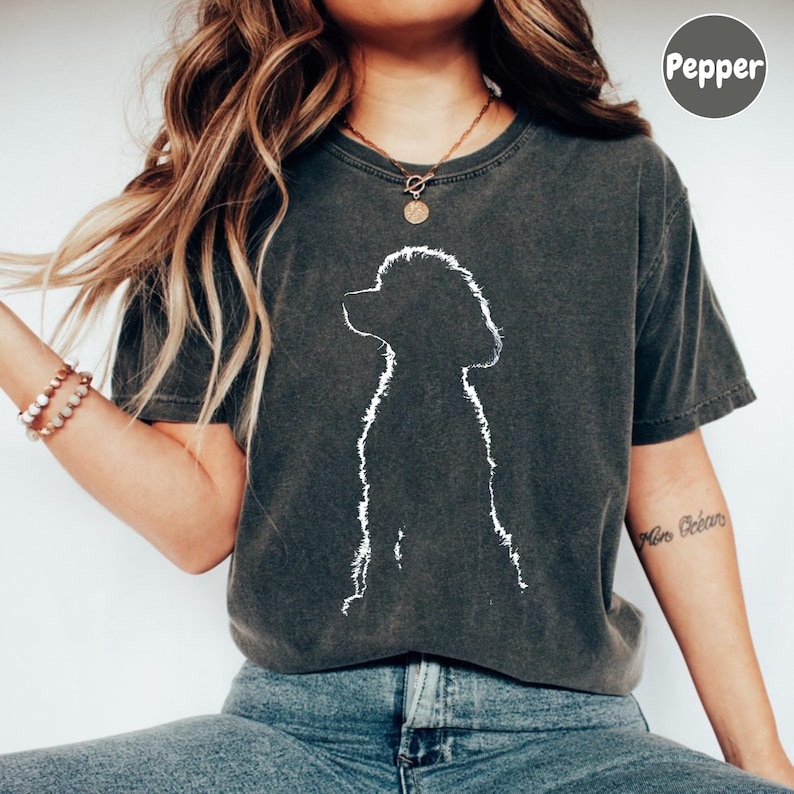A woman wearing a gray t-shirt with a white silhouette of a dog, paired with blue jeans, and accessorized with bracelets and a necklace.
