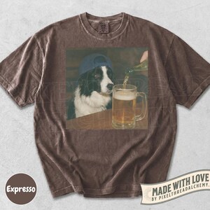 May include: Brown t-shirt featuring a graphic of a Border Collie wearing a blue cap, watching beer being poured into a pint glass. The shirt has a vintage look, with the word "Expresso" on the bottom left.