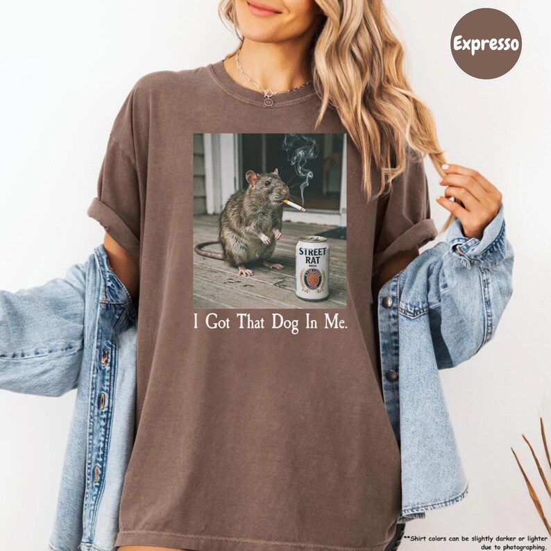 A woman wearing a brown t-shirt with a graphic of a dog smoking a cigarette and the text "I Got That Dog In Me" printed on it.