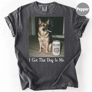 A German Shepherd dog sitting on a wooden floor next to a can of Miller Lite beer, with the text "I Got That Dog In Me."